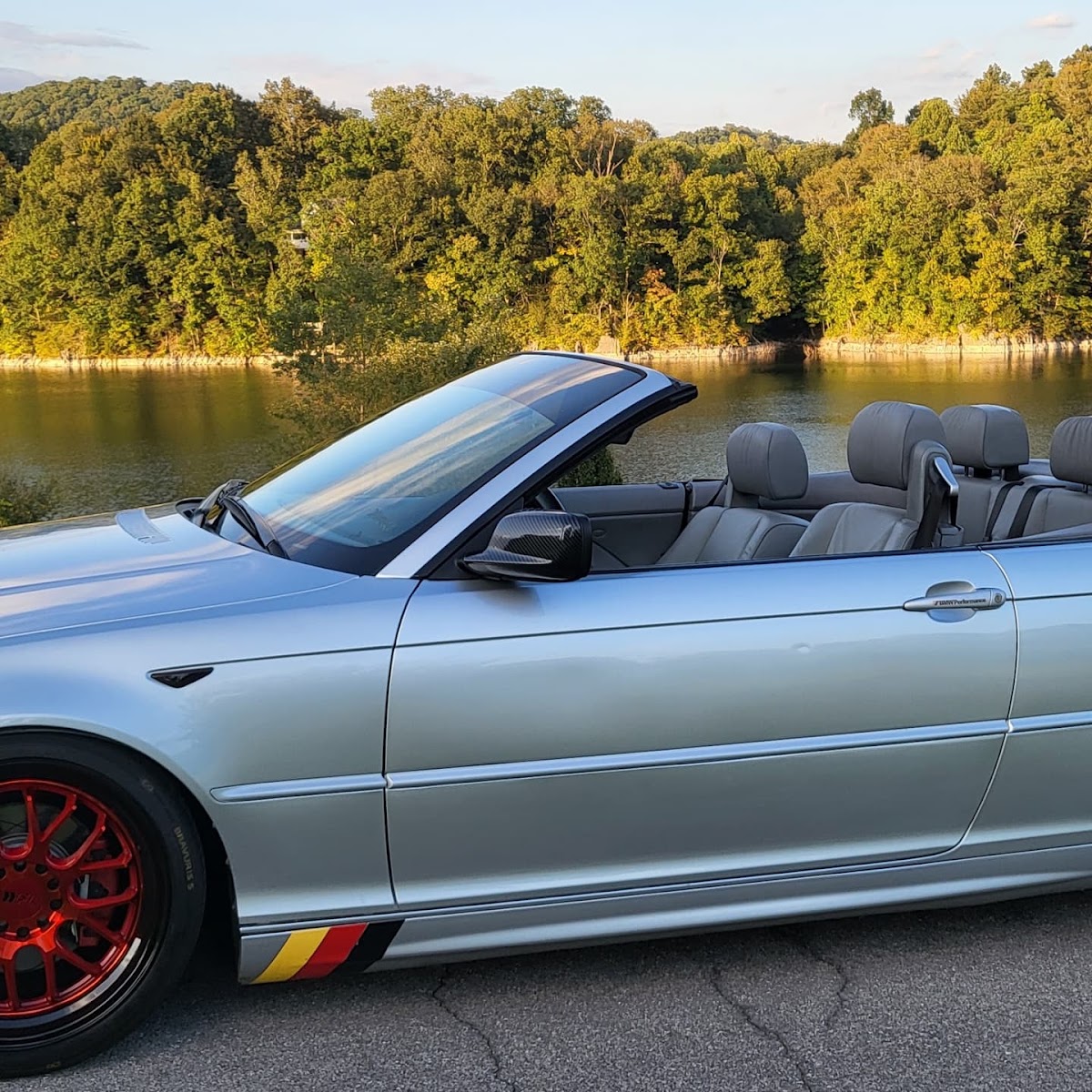 Silver BMW convertible with red wheels parked by a lake in the East Tennessee hills