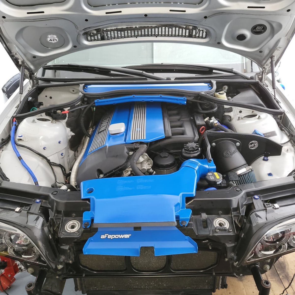 Engine bay of a BMW with a blue engine cover and aFe Power intake, hood up in the shop